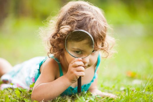 Kid plays with magnifying glass in the garden