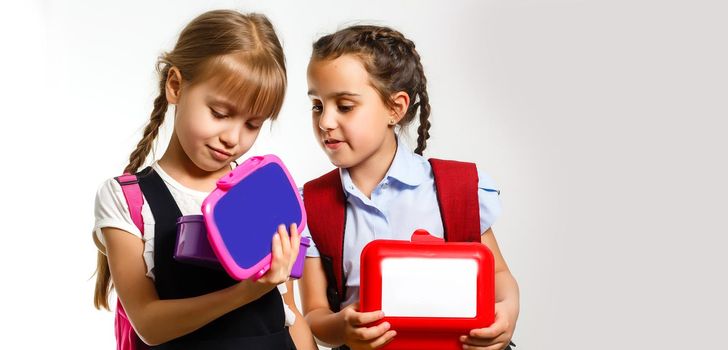 Pupils of primary school with lunch-boxes in hands. Girls with backpacks are eating fruit. Beginning of lessons. First day of fall.