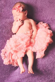 Newborn pretty baby girl in pink tutu dress sleeps on the purple textile