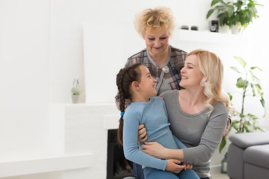 Three generations of women. Beautiful woman and teenage girl are kissing their granny while sitting on couch at home