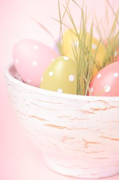 Decorative eggs in pot with grass over pink background. Easter decor.