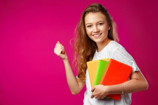 Portrait of a girl student holding many books and gesturing 'yes' against pink background