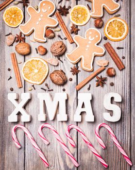 Gingerbreads with spices on the wooden table, wooden letters XMAS and Santa staffs candies. Christmas aroma decor