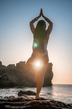 Young woman in swimsuit with long hair practicing stretching outdoors on yoga mat by the sea on a sunny day. Women's yoga fitness pilates routine. Healthy lifestyle, harmony and meditation concept.