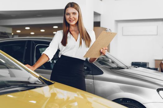 Attractive young female car dealer standing in showroom near a new car