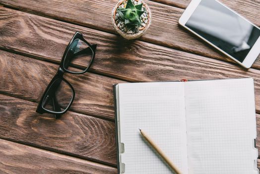 Blank notepad with pen, glasses, smartphone and succulent plant on a wooden table. Concept of freelance working place.