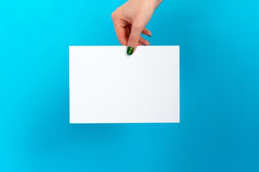 Woman hand holding blank card on blue background, close up.