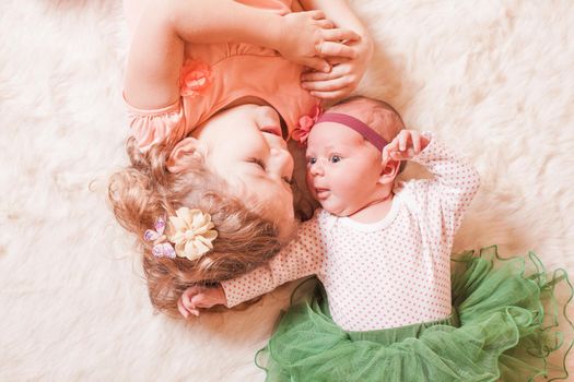 Little girl with her newborn sister on a fur carpet