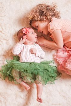 Little girl with her newborn sister on a fur carpet