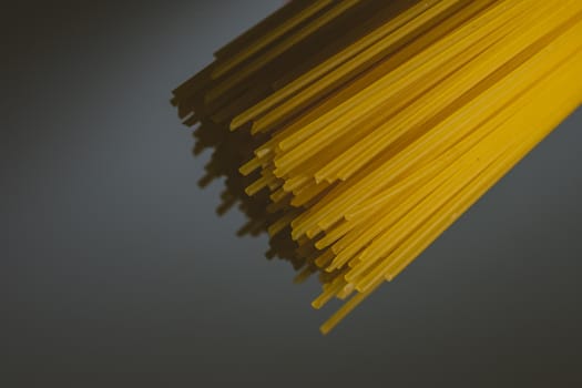 Cluster of long and thin spaghetti on a dark background with backlight. Raw pasta. Culinary topics.