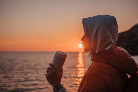 woman traveler drinks coffee with a view of the mountain landscape. A young tourist woman drinks a hot drink from a cup and enjoys the scenery in the mountains. Trekking concept