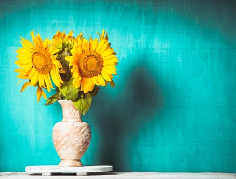 Sunflower in the vase over blue wooden background