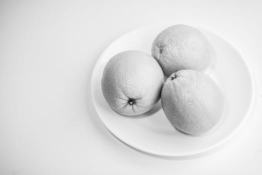 Three oranges in a plate on a white background. Black and white photo. Still life. Selective focus.