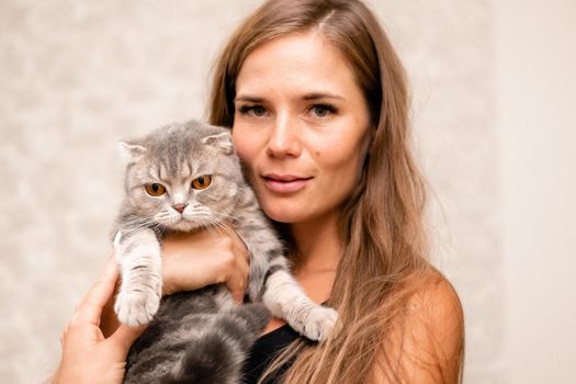 Attractive girl embracing her pet with smile. Indoor portrait of cute ginger woman playing with cat.