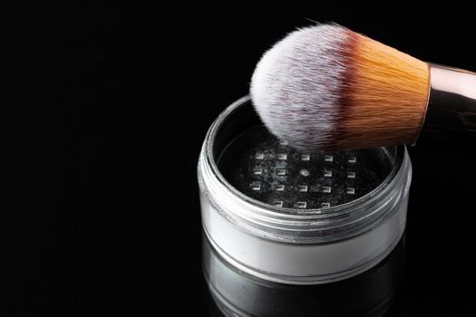 Make up powder with brush on black background, close up.