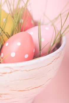 Decorative eggs in pot with grass over pink background. Easter decor.