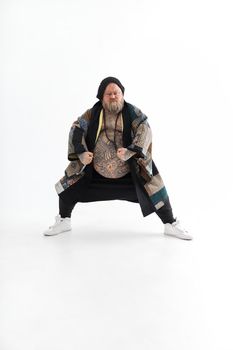 Fat stylish bearded tattoed caucasian man with big belly is posing and dancing wearing ethnic kimono