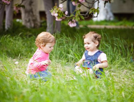 Two girls play in the garden, sitting on the grass