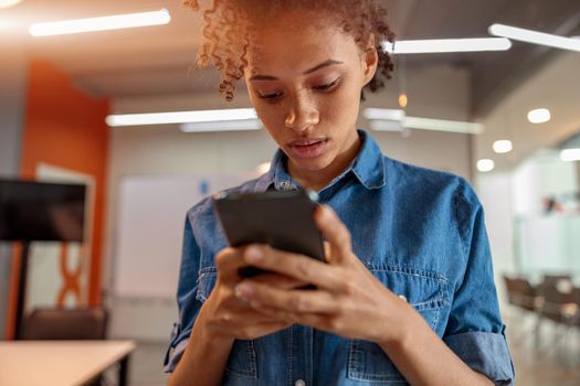 Close up of young businesswoman holding smartphone and looking on screen in the office