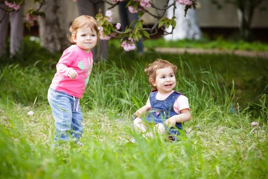 Two girls play in the garden, sitting on the grass