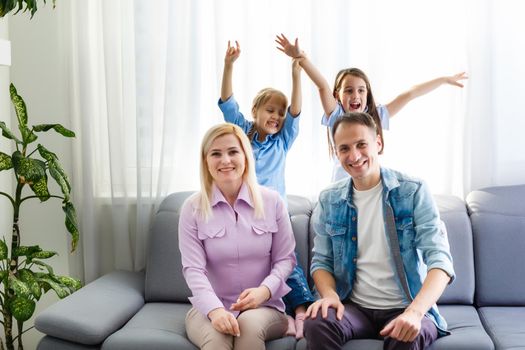 Cheerful young family with kids laughing sitting on couch together, parents with children enjoying entertaining at home