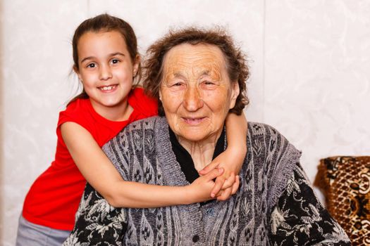 Family bonding concept. Lovely little girl happily emracing her grandma in light living room