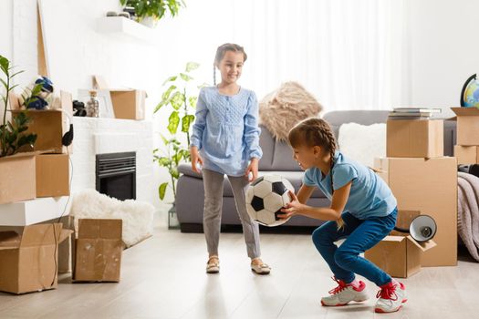 two little daughters celebrating moving day, excited by relocation into new house, laughing living room with cardboard boxes