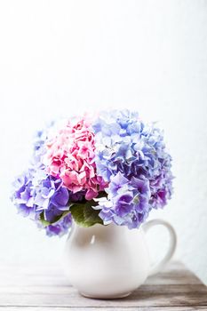 Hydrangea flowers in a white jug on the shabby wooden table