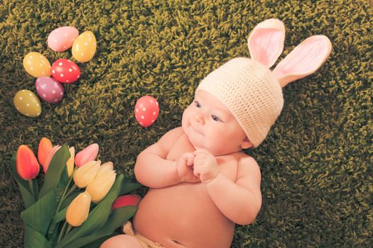 Three months baby lying on on the grass carpet as a Easter bunny