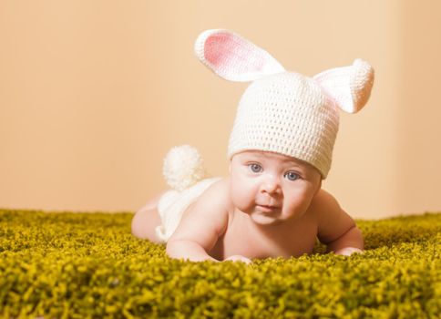 Three months baby lying on his stomach as a Easter bunny on the grass carpet