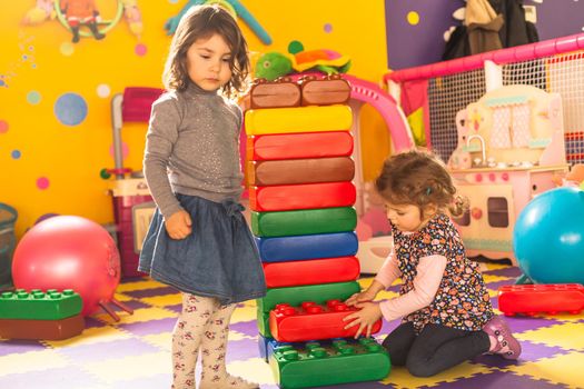 Two girls play with big bricks in playroom