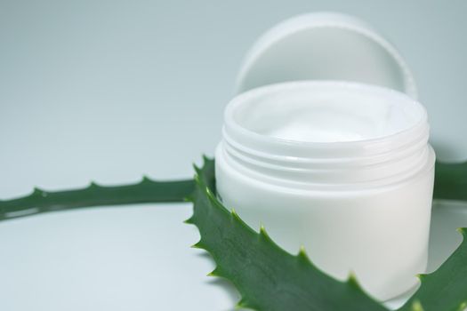 A white jar of cream is decorated with aloe leaves. Side view. Cosmetic theme.