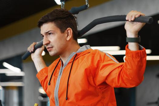 Young man in orange windbreaker working out training back muscles in the gym