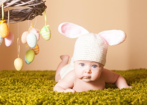 Three months baby lying on his stomach as a Easter bunny on the grass with eggs