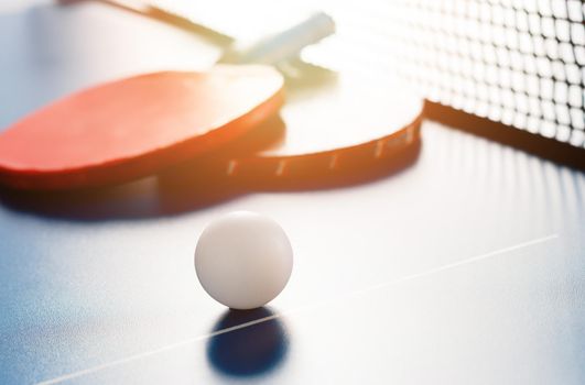 Two tennis rackets and a white ball lie on a tennis table near the net. Active recreation and playing ping pong. Sports background.