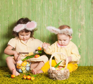 Little boy and girl as a Easter rabbits on the grass with colorful eggs