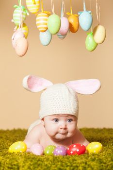 Three months baby lying on his stomach as a Easter bunny on the grass with eggs