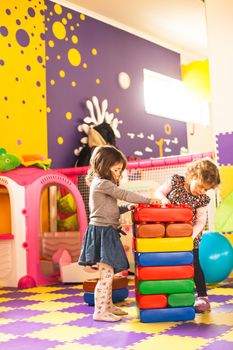 Two girls play with big bricks in playroom