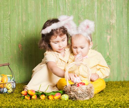 Little boy and girl as a Easter rabbits on the grass with colorful eggs