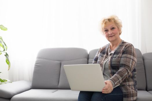 Elderly woman sitting at home, using laptop computer, smiling.