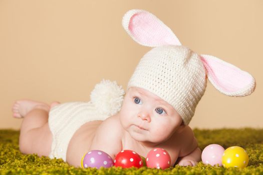 Three months baby lying on his stomach as a Easter bunny on the grass with eggs