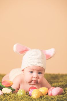 Three months baby lying on his stomach as a Easter bunny on the grass with eggs