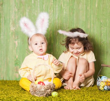 Little boy and girl as a Easter rabbits on the grass with colorful eggs