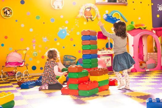 Two girls play with big bricks in playroom