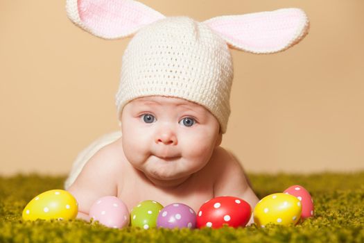 Three months baby lying on his stomach as a Easter bunny on the grass with eggs