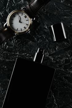 Men's watches and an open bottle of black eau de toilette lie on a dark textured background. Fragrance for men. flat lay