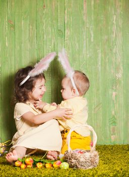 Little boy and girl as a Easter rabbits on the grass with colorful eggs