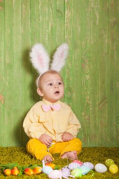 Little boy as a Easter rabbit on the grass with colorful eggs
