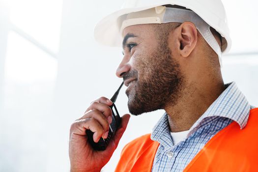 Young construction worker in uniform using walkie talkie on site, close up portrait