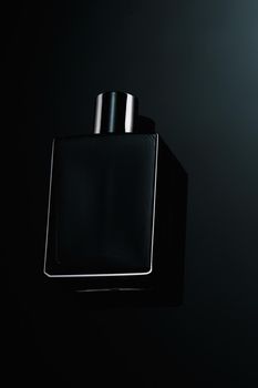 Silhouette of a black bottle of eau de toilette for men on a dark background. Advertising photo of perfumes. Dark style. Layout.